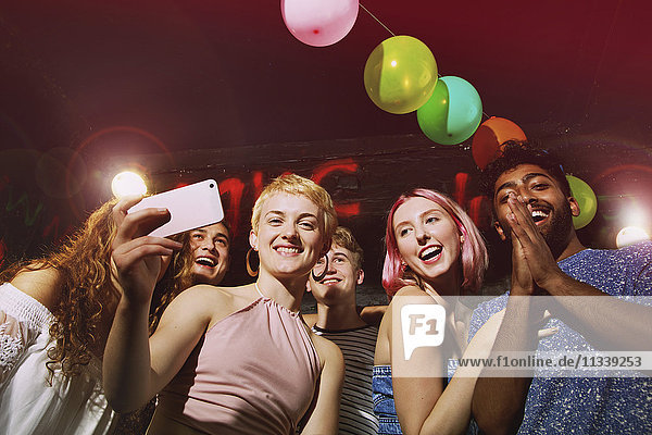 Low angle portrait of happy woman taking selfie with friends at yard