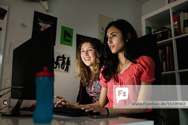 Fröhliches Teenagermädchen mit Computer und Freund in der Dunkelkammer zu Hause
