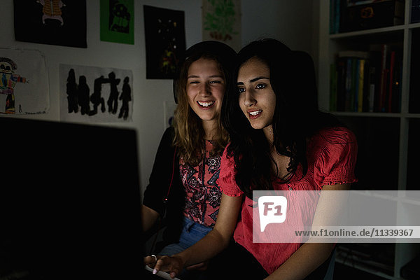 Glückliche Teenager-Mädchen die den Computer in der Dunkelkammer zu Hause benutzen.