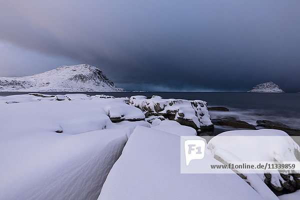 Storm clouds on the snowy peaks reflected in the cold sea at night Haukland Lofoten Islands Northern Norway Scandinavia Europe