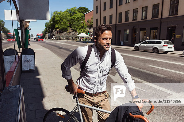 Nachdenklicher Geschäftsmann steht mit dem Fahrrad auf dem Bürgersteig in der Stadt.