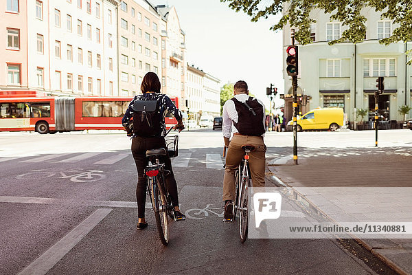 Rückansicht von Geschäftsleuten  die auf der Stadtstraße Fahrrad fahren