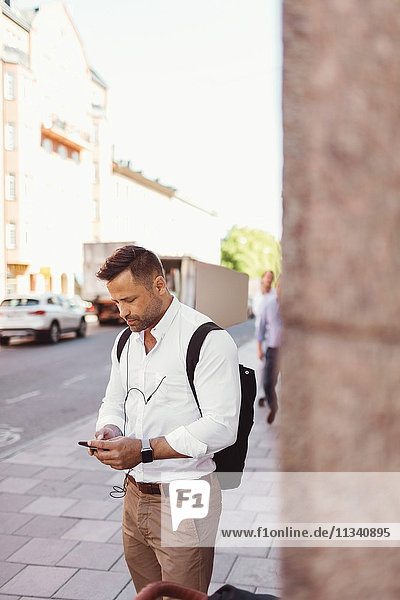 Geschäftsmann mit Smartphone im Stehen auf dem Bürgersteig