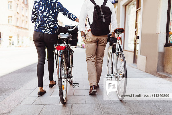 Niederquerschnitt Rückansicht von Geschäftskollegen  die mit Fahrrädern auf dem Bürgersteig gehen