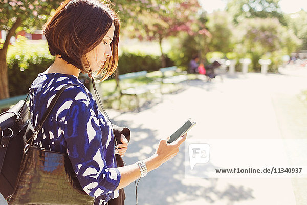 Seitenansicht der Geschäftsfrau mit Smartphone auf dem Fußweg bei Sonnenschein