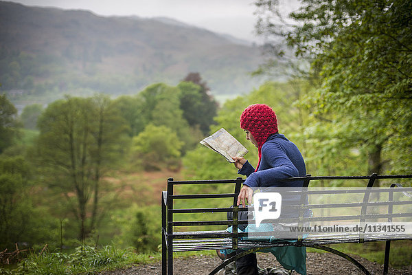 Eine Frau ruht sich bei einem Spaziergang im Lake District in der Nähe von Grasmere  Cumbria  England  Vereinigtes Königreich  Europa  auf einer Bank aus.