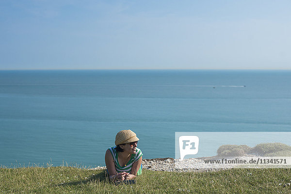 Eine Frau liegt auf den Klippen bei Beachy Head mit Blick auf das Meer in der Ferne  East Sussex  England  Vereinigtes Königreich  Europa