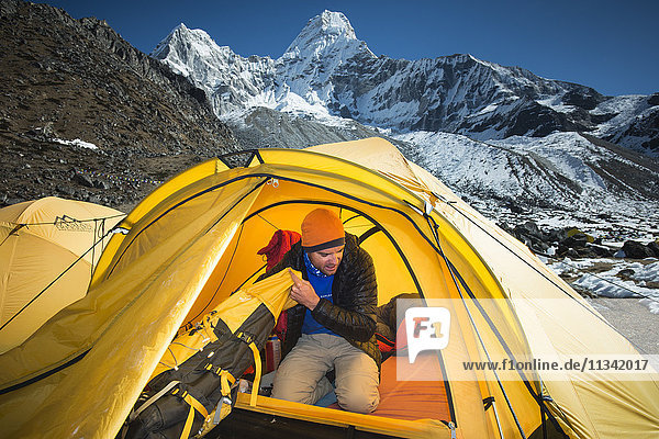 Ein Bergsteiger packt seinen Rucksack in Vorbereitung auf die Besteigung der Ama Dablam  dem 6856 m hohen Gipfel in der Ferne  Khumbu-Region  Himalaya  Nepal  Asien
