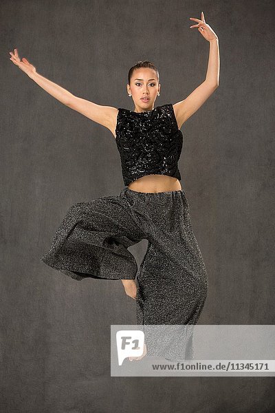 Attractive young woman dancing full length in black top and baggy gray pants in studio shot on gray background.