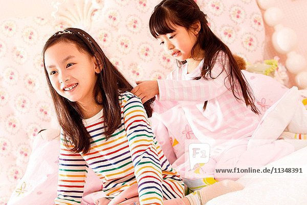 Two little girls are playing on the bed