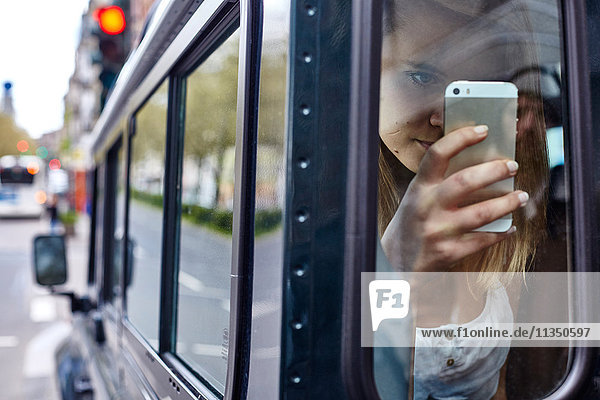 Junge Frau hinter einem Autofenster schaut auf ihr Handy