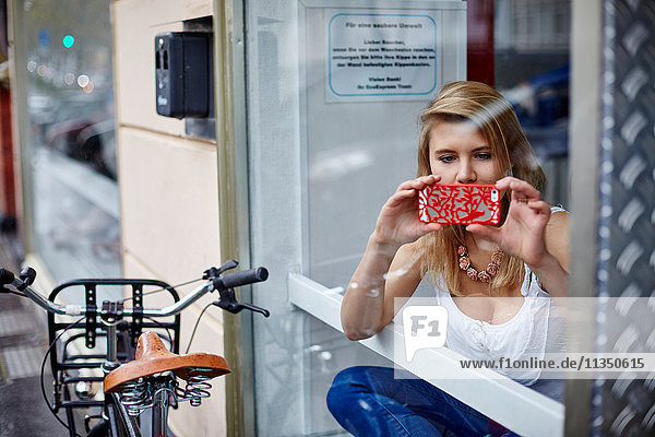 Young woman with cell phone behind window pane