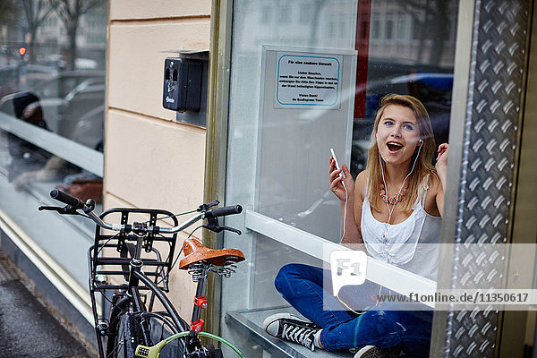 Fröhliche junge Frau hinter einer Fensterscheibe hört Musik