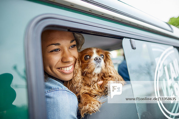 Fröhliche junge Frau mit Hund im Auto schaut aus dem Fenster