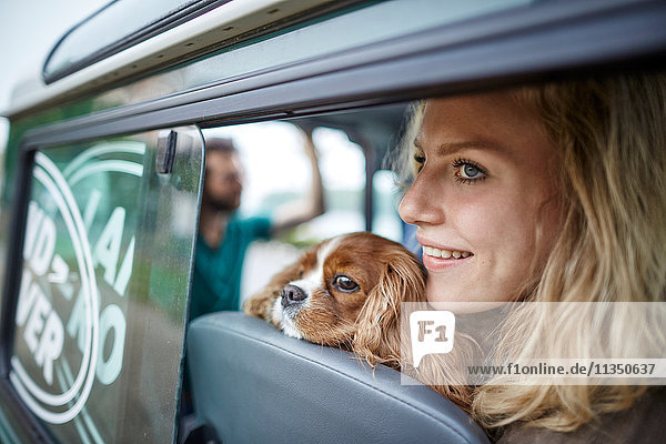 Lächelnde junge Frau mit Hund im Auto schaut aus dem Fenster