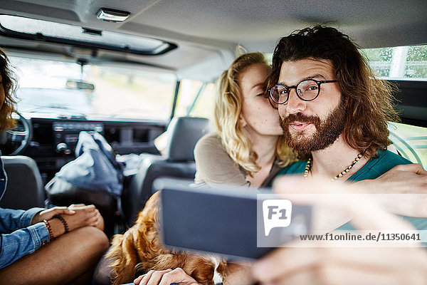 Happy couple with dog taking a selfie in car