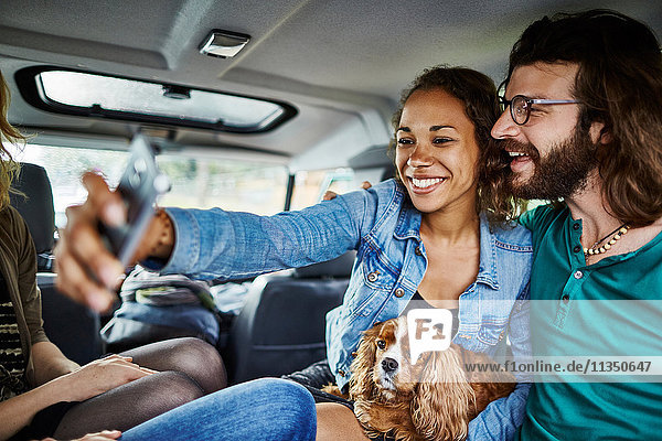 Fröhliches Paar mit Hund macht ein Selfie im Auto