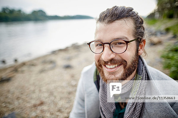 Lächelnder junger Mann mit Vollbart am Flussufer