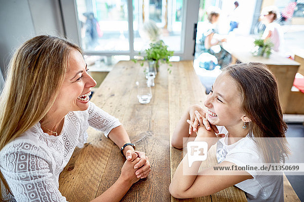Glückliche Mutter und Tochter sitzen im Restaurant gegenüber