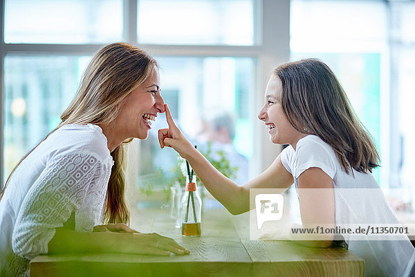 Verspielte Mutter und Tochter sitzen im Restaurant gegenüber