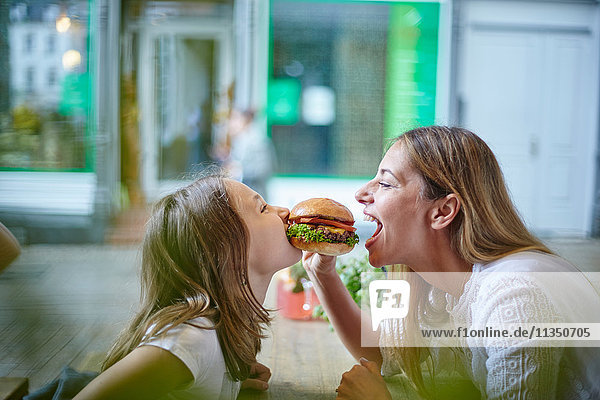 Mutter und Tochter im Restaurant teilen sich einen Hamburger