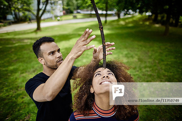 Junge Frau mit ihrem Freund im Park balanciert einen Stock auf ihrem Kopf