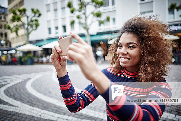 Lächelnde junge Frau in der Stadt macht ein Selfie