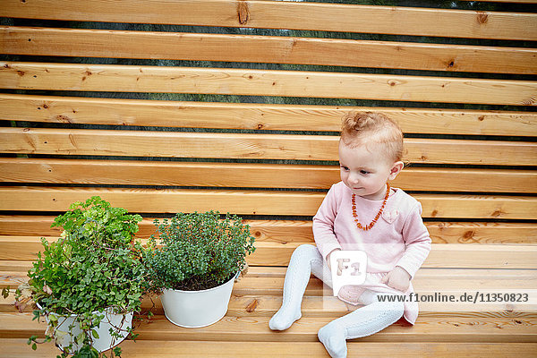 Baby girl sitting on bench next to potted plants
