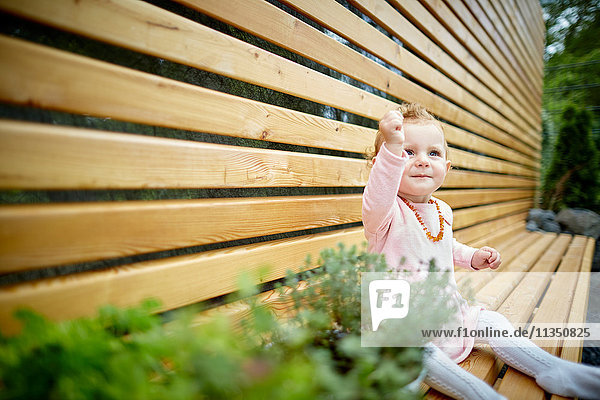 Baby girl sitting on bench next to potted plants