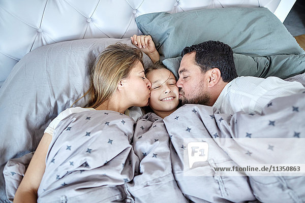 Parents kissing daughter in bed