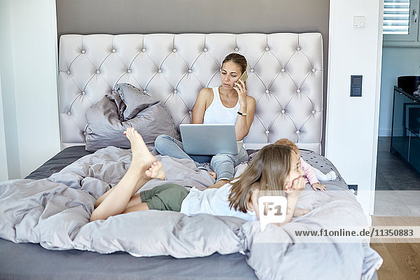 Mother with laptop and daughter and baby girl in bed