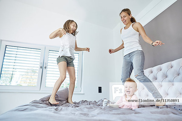 Mother with daughter and baby girl jumping on bed