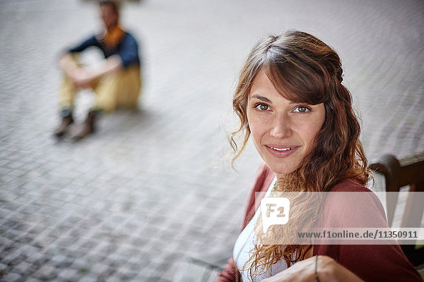 Portrait einer lächelnden jungen Frau mit Mann im Hintergrund