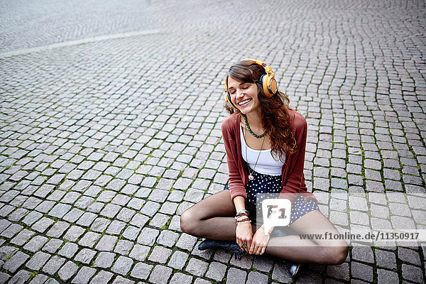 Fröhliche junge Frau sitzt auf einem Platz und hört Musik