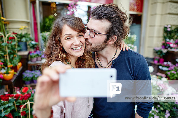 Lächelndes junges Paar macht ein Selfie vor einem Blumengeschäft