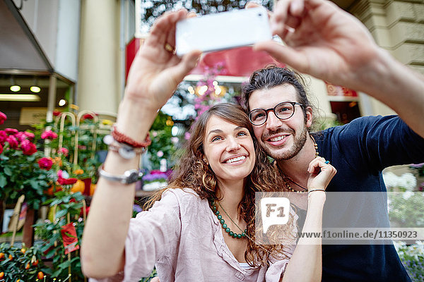 Smiling young couple taking a selfie in front of a flower shop