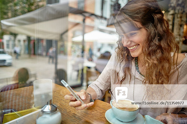 Lächelnde junge Frau in einem Cafe schaut auf ihr Handy
