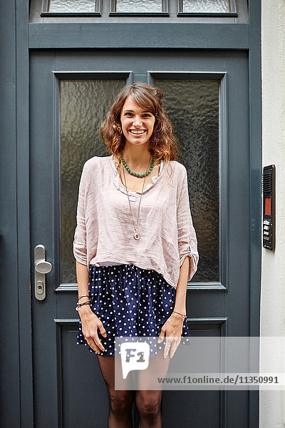 Portrait of smiling young woman standing at a door