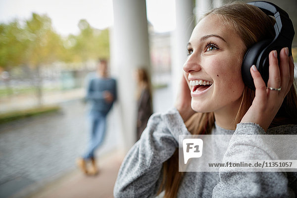 Fröhliche junge Frau mit Kopfhörern im Freien