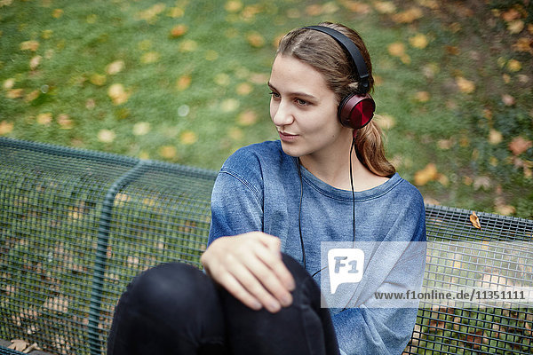 Junge Frau mit Kopfhörern auf einer Parkbank
