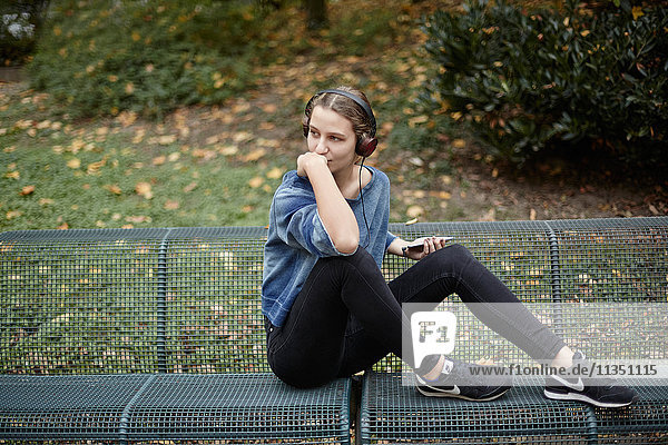 Junge Frau mit Kopfhörern auf einer Parkbank