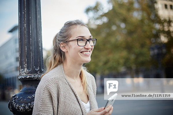 Lächelnde junge Frau mit Handy schaut zur Seite