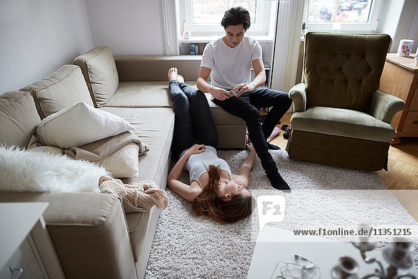 Junger Mann macht ein Handyfoto seiner Freundin auf dem Fußboden