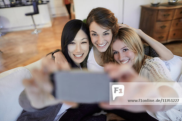 Three happy women sitting on couch taking a selfie