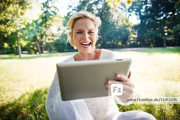 Lachende reife Frau mit Tablet-PC im Park