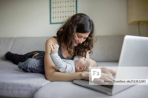 Woman with baby on couch using laptop