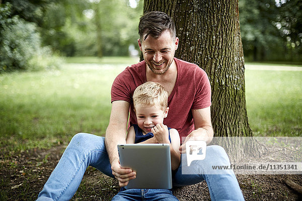 Glücklicher Vater und Sohn im Park schauen auf Tablet