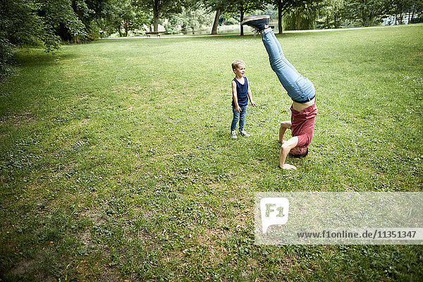 Boy looking at father doing a headstand in meadow