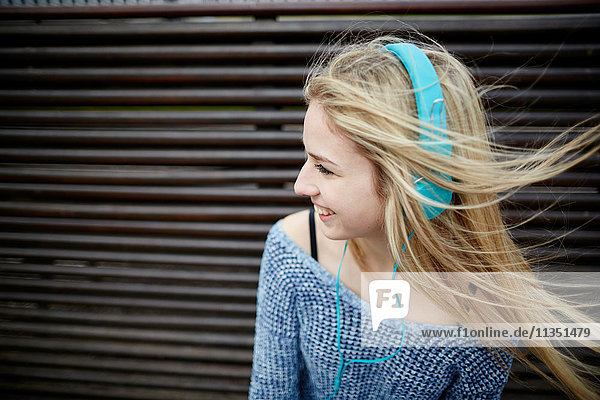 Happy young woman wearing headphones on bench
