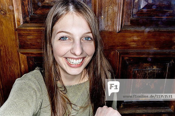 Portrait of smiling young woman in front of wooden door